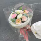 Bouquet of pink and cream roses, carnations, gerberas, and eucalyptus in cellophane with pink ribbon.