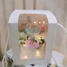 White gift box with a candle and flowers, illuminated by fairy lights.