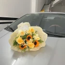 Bouquet of sunflowers, yellow roses, and daisies on a car hood.