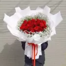 Bouquet of red roses with baby's breath, wrapped in white paper and tied with red ribbon.