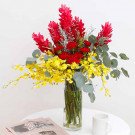 Red ginger, yellow dancing orchids, red carnations, and eucalyptus in a glass vase.