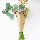 A hand holds a bouquet of spring flowers in a brown paper cone holder.