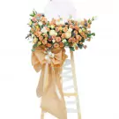 A tall bouquet of peach and white roses, chrysanthemums, and other flowers on a wooden stand with a large peach bow.