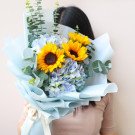 A bouquet of sunflowers and hydrangeas in light blue paper wrap.