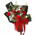 Red roses, carnations, pinecones, and eucalyptus in a black bouquet with a red burlap bow.