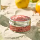 Red scented candle tin with "Without You" text and floral design, surrounded by sand.