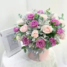Pink and purple roses in a pink box with a silver ribbon and a book.