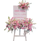 Flower stand with pink roses, white flowers, and a congratulatory sign.