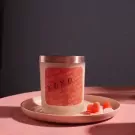 Candle with "XOXO" on the label, on a pink saucer with heart-shaped candies.