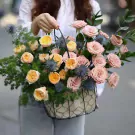 Basket of pink and yellow roses, blue thistles, and green foliage.