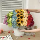 Vibrant rainbow flower box with roses, sunflowers, hydrangeas, and greenery.