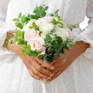 Bride holding a bouquet of pink and white roses with greenery.