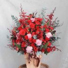 Large floral arrangement of red roses, carnations, and greenery in a woven basket with a ribbon.