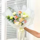 Rainbow roses and other flowers in a bouquet wrapped in white paper, held by a hand.