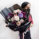 A woman holding a bouquet of purple and pink flowers wrapped in black paper.