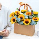 Brown paper gift bag filled with sunflowers and eucalyptus, tied with an orange ribbon.