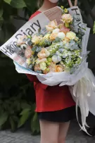 A bouquet of peach roses, hydrangeas, and carnations wrapped in newspaper and white paper.