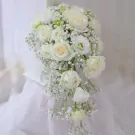 Cascading bouquet of white roses and baby's breath on a white cloth.