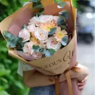 A bouquet of pink roses, gerbera daisies, and eucalyptus in kraft paper with "Gorgeous You" text.
