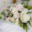 A bridal bouquet of white roses, pink tulips, and delicate filler flowers on a white lace cloth.