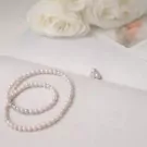 Pearl necklace and earrings with white roses in the background.
