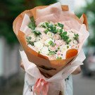 A bouquet of pink and white roses, carnations, and greenery, wrapped in brown paper.