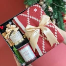 Christmas gift box with red scarf, berry bliss candle, and matches, tied with a gold ribbon.