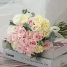 Pink and cream roses and carnations in a bridal bouquet, tied with ribbon, resting on books.
