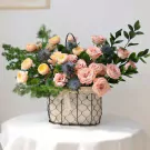 Pink and peach roses, blue thistles, and greenery in a wire basket.