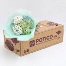 A bouquet of white daisies and blue and green hydrangeas in light blue wrapping sits on a cardboard box.