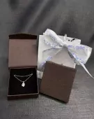 Heart-shaped stone necklace in open gift box beside a gift bag with snowflake ribbon.