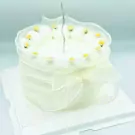 Delicate white cake with sheer ruffled trim and tiny yellow-topped white flowers.