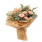 Peach roses, baby's breath, and eucalyptus in brown paper wrapping, tied with twine.