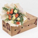 Bouquet of orange and yellow carnations in beige wrapping, placed on a cardboard box.