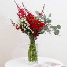 Red orchids, carnations, and white chrysanthemums in a clear vase with eucalyptus.