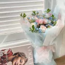 A bouquet of pink and blue roses with delicate baby's breath, wrapped in pale blue paper with a pink ribbon.