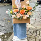 Basket of orange and pink roses with baby's breath and greenery.