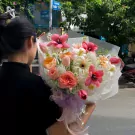 A person holds a vibrant bouquet of pink tulips, orange roses, and white gerbera daisies.