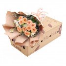 Peach roses and white flowers in a bouquet on a cardboard box.