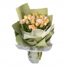 Bouquet of cream, pink, and yellow roses with baby's breath, wrapped in green and white paper.