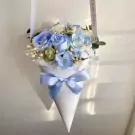 A pastel blue and white floral bouquet in a white cone with a blue ribbon.