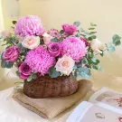 Basket of pink and purple chrysanthemums and roses with eucalyptus leaves.