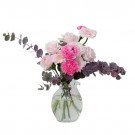Pink roses, carnations, and gerbera daisies in a glass vase with eucalyptus leaves.