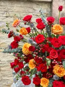 A large floral arrangement of red and orange roses with eucalyptus and red berries.