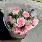 A bouquet of pink roses, white flowers, and greenery wrapped in textured white paper.