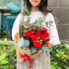Red roses and carnations bouquet with eucalyptus, wrapped in brown paper and tied with a red ribbon.