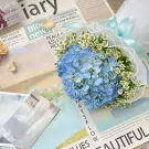 Blue hydrangea and white daisies bouquet with pearls on newspapers.