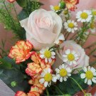 Pink roses, orange carnations, and white daisies in a bouquet.