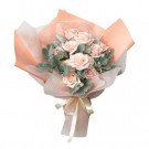 Pink rose bouquet with dusty green leaves, wrapped in peach and white paper with a cream ribbon.