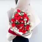 Red roses and white daisies in a bouquet wrapped in cream paper.